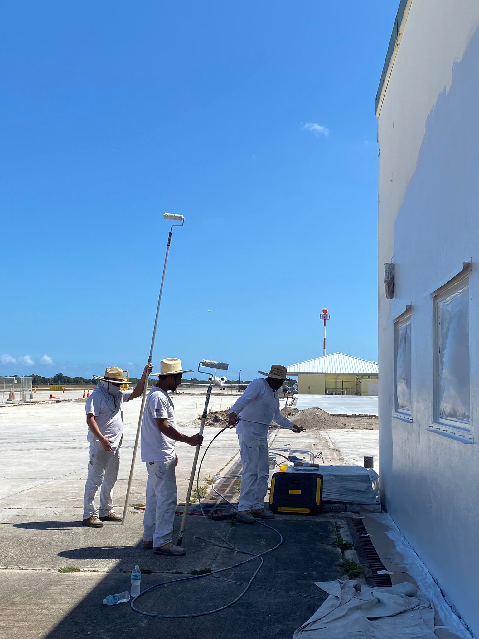 Crew spray painting exterior wall at airport hangar