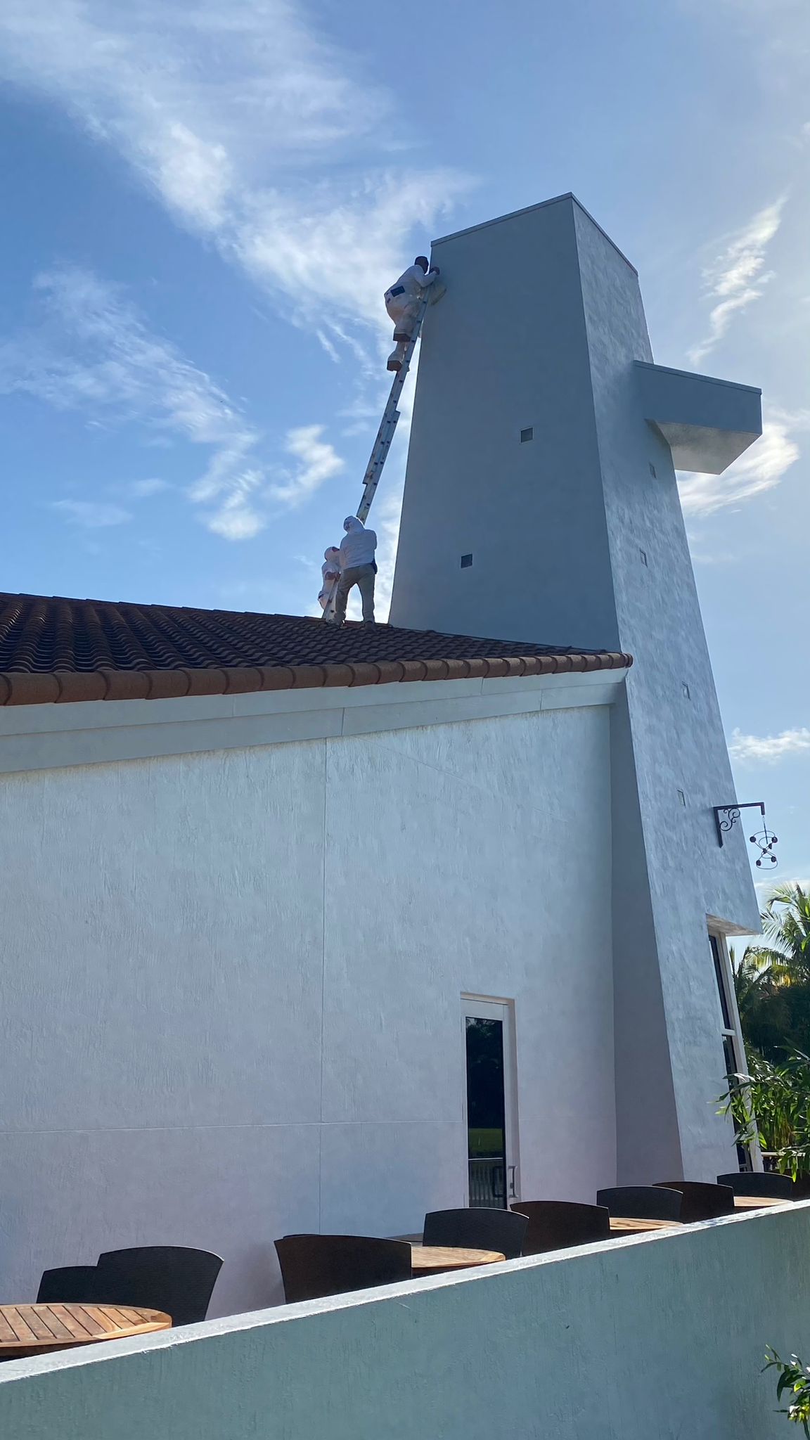Crew on extension ladder painting tall commercial tower