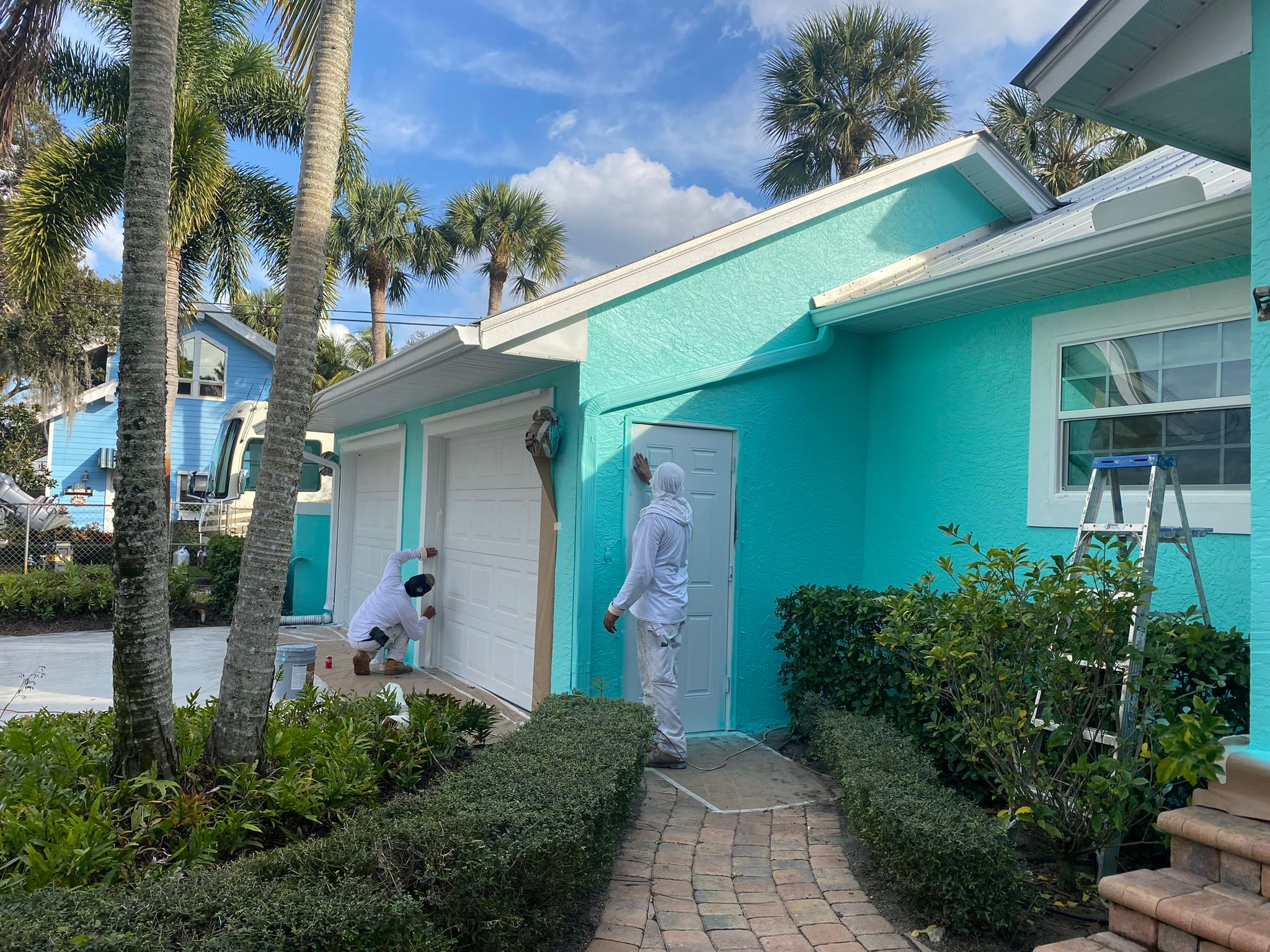 Crew members painting garage door and trim of a teal house