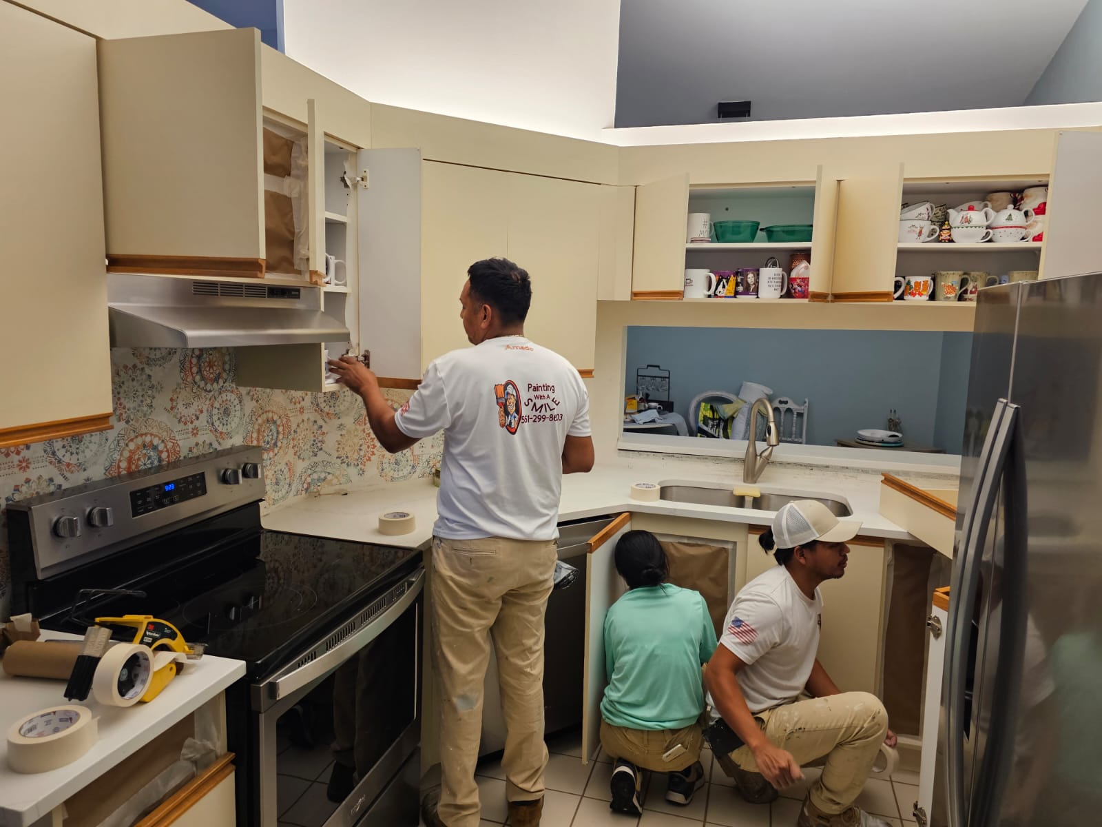 Crew member prepping cream-colored cabinets before painting