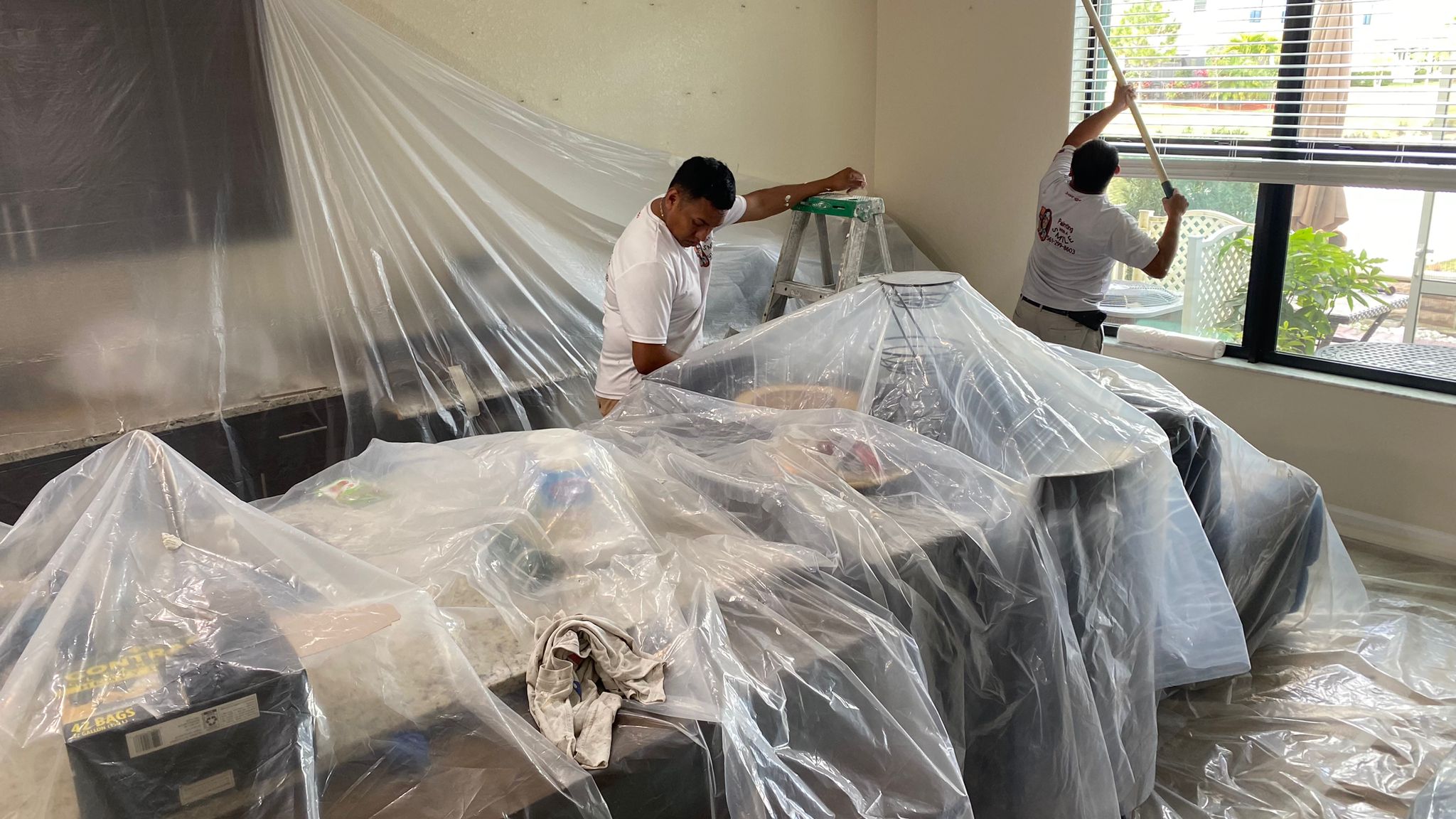 Crew carefully masking furniture with plastic before painting